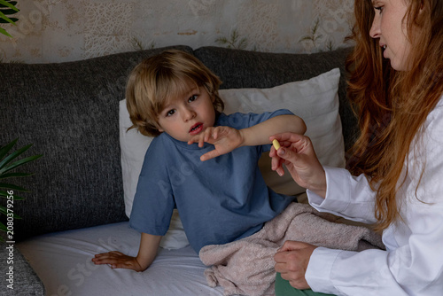 Slika na platnu The mother takes care of the sick child, taking his temperature and giving him pills