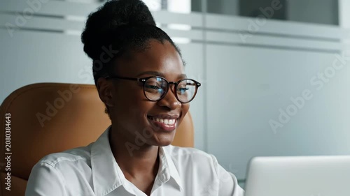 Smiling African American Businesswoman Working on Laptop in Modern Office Environment.