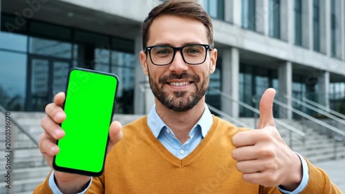 Smiling Young Man with Glasses Showing Green Screen Smartphone and Thumbs Up Gesture.