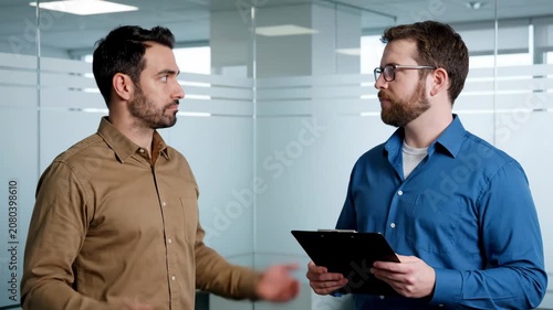 Two serious businessmen discussing work in a modern office environment, focusing on collaboration and problem-solving.