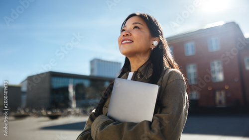 Young female student commuting to university smiles while holding laptop