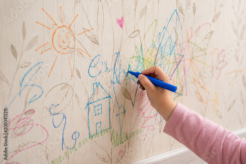 Close up of child drawing colorful crayon scribbles on wallpaper causing damage to wall at home