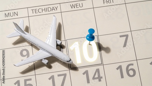 Toy airplane on calendar with blue pin marking travel date