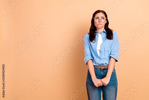 Photos Nervous young woman biting her lip and looking unsure in casual blue shirt and j