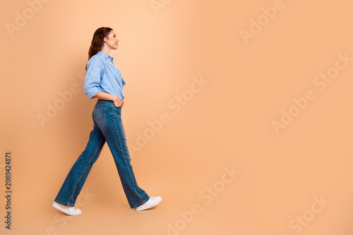 Photography Woman walking in profile across a peach background wearing blue shirt and jeans,