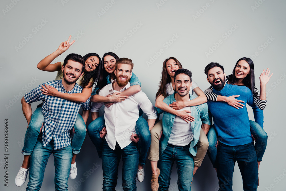 Fototapeta premium Happy group of friends enjoying piggyback rides and laughing together in casual clothing, young adults having fun and celebrating friendship in a studio portrait