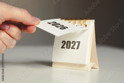 Turning the page from 2026 to 2027 – New Year calendar concept with hand and desk flip calendar	
