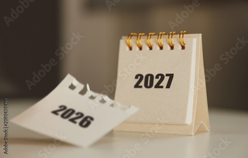 Turning the page from 2026 to 2027 – New Year calendar concept with hand and desk flip calendar	
