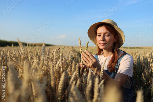Woman in straw hat inspecting ripe wheat stalks in a golden field at sunset