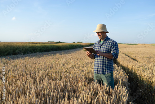 Farmer in straw hat using tablet computer in golden wheat field at sunset