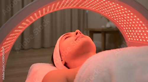 Woman Receiving Red Light Therapy Treatment for Skin Care, Close-up of Face Under LED Light Ring, Professional Beauty Salon Facial Procedure