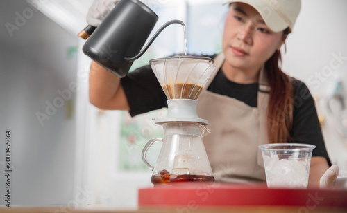 Slika na platnu Young Asian barista carefully prepares handcrafted pour-over coffee using a gooseneck kettle in a modern coffee shop, emphasizing specialty coffee craftsmanship