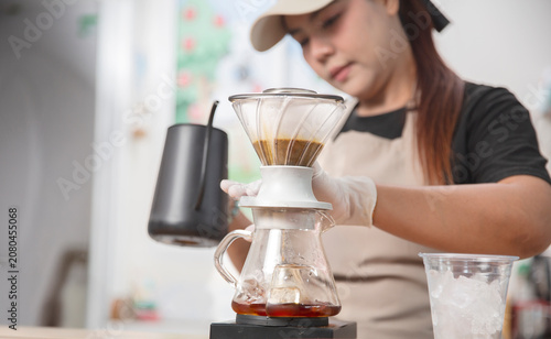 Fotografija Young Asian barista carefully prepares handcrafted pour-over coffee using a gooseneck kettle in a modern coffee shop, emphasizing specialty coffee craftsmanship
