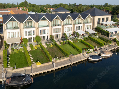 Aerial view of luxury riverside homes with manicured lawns, private boat moorings, and modern architecture along the river Thames in Maidenhead, England, United Kingdom.
