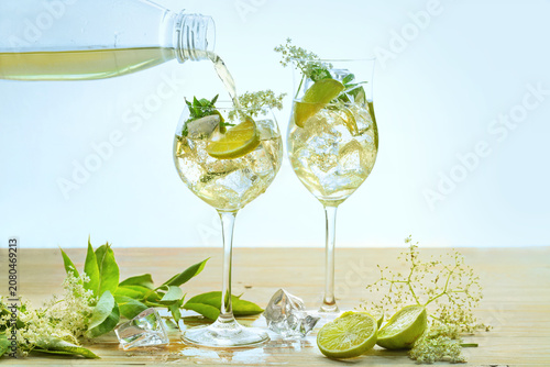Refreshing summer drink called Hugo Spritz is poured in two wine glasses, cocktail from prosecco, elderflower, syrup, soda, mint and lemon slices, light background, copy space