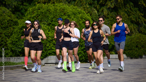 Tableau sur toile Large running club jogging together on sunny park path
