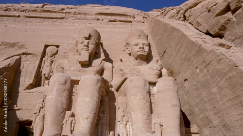 Low angle view of the massive stone statues of Ramses II at the ancient Abu Simbel Temple in Aswan, Egypt, featuring intricate carvings and hieroglyphs.