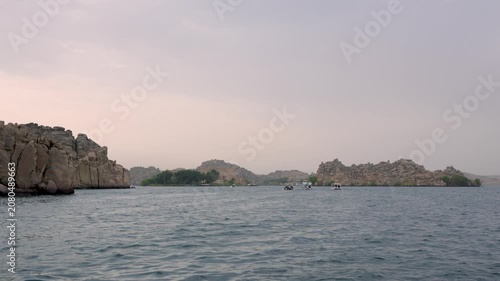 A scenic view of the ancient Philae Temple complex on Agilkia Island in Aswan, Egypt, seen from a small boat on the Nile River.