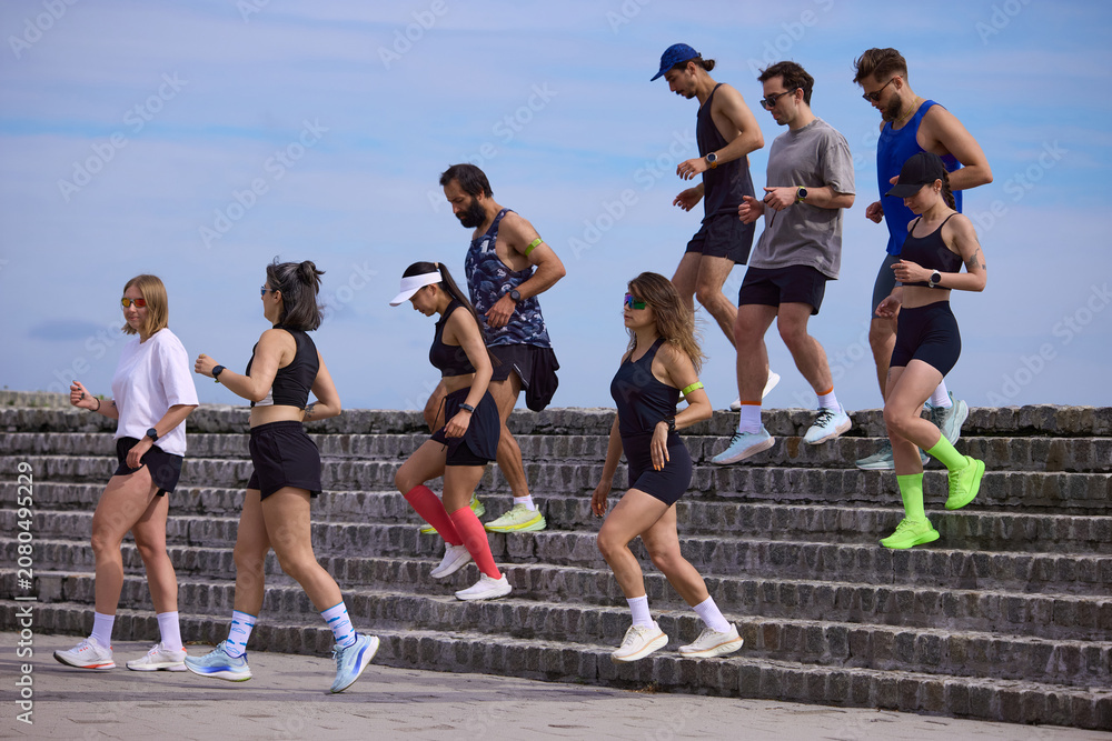 Fototapeta premium Mixed running club going down stone steps after outdoor training session. Concept of recovery pace, team fitness, urban cardio, endurance practice and healthy active lifestyle.