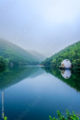 Misty mountain lake with egg-shaped house reflection