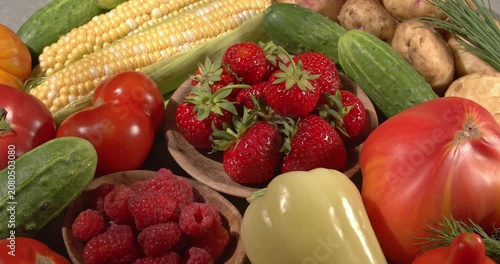 Fresh healthy products on a gray table. Hand puts strawberries in a wooden plate. Close-up footage of  corn, strawberries, cucumbers, tomatoes, green onions, potatoes, raspberries, dill, sweet peppers