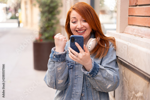 Foto Excited redhead woman celebrating good news on smartphone