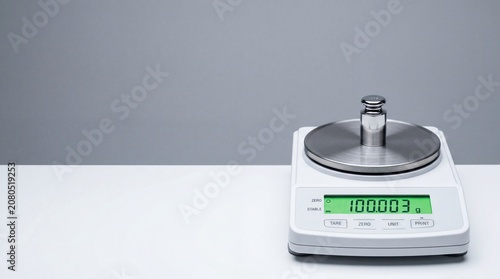 Digital scale displaying weight measurement with a calibration weight on the platform. The background is plain and neutral in color.
