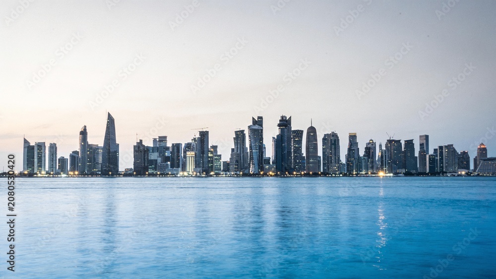 Fototapeta premium A serene evening cityscape with a calm body of water reflects the urban skyline at dusk.