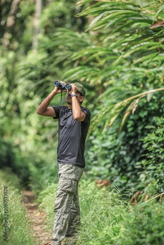 Nature lover exploring a lush tropical forest with binoculars in the Western Ghats of Munnar, India, embracing eco-tourism and adventure