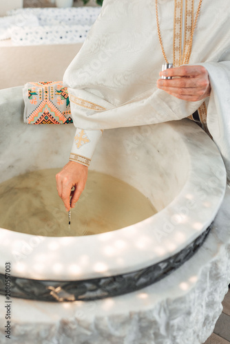Foto Priest blessing holy water in a marble font during a baptism ceremony