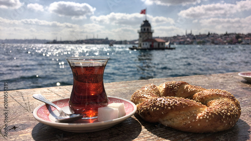 Traditional turkish tea in a glass with a sesame bagel on a wooden table overlooking the bosphorus and Maidens Tower in Istanbul