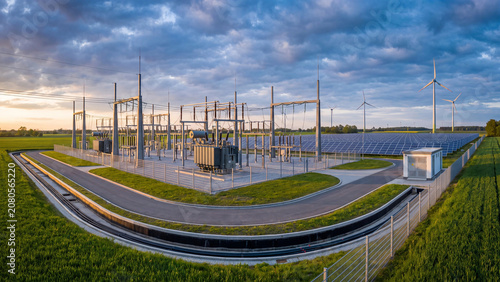 Aerial view of electrical power substation with transformers solar panels and wind turbines at sunset showing renewable energy grid infrastructure clean electricity distribution and sustainable
