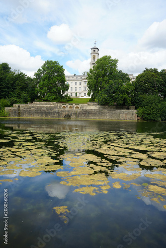 View Of The Historic Trent Building And Its Clock Tower Reflecting In The Lake At Highfields Park, Nottingham, England With Surface Algae.