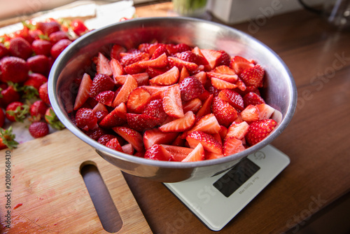 preparing berries for the winter during the season, on the kitchen countertop are washed strawberries and a bowl with sliced berries on the scales
