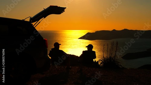 Two silhouetted men packing camping chairs after sunset. Two silhouetted men packing up their camping chairs next to a car with an open trunk after enjoying a stunning golden sunset over the ocean