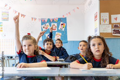 Young students actively participating in a bright classroom, raising hands to answer questions and engaging in learning