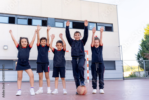 Diverse group of elementary students in school uniforms cheering with arms raised on a school playground, expressing joy and teamwork
