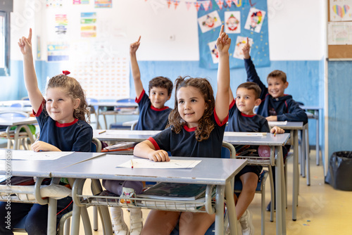 Young students actively participating in a school lesson, raising hands to answer questions and showing engagement in the classroom