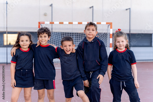 Group of smiling young students in sports uniform standing on an outdoor playground with a goal post