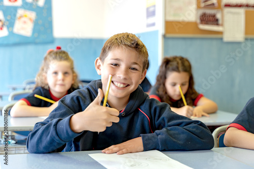 Cheerful primary school boy sitting at a desk, smiling and showing a thumbs up gesture during a lesson