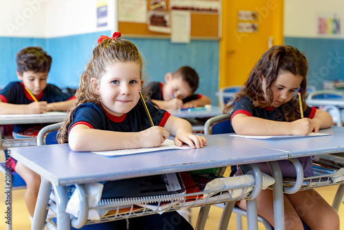 Young students in school uniform sitting at desks, writing on paper during an elementary education lesson