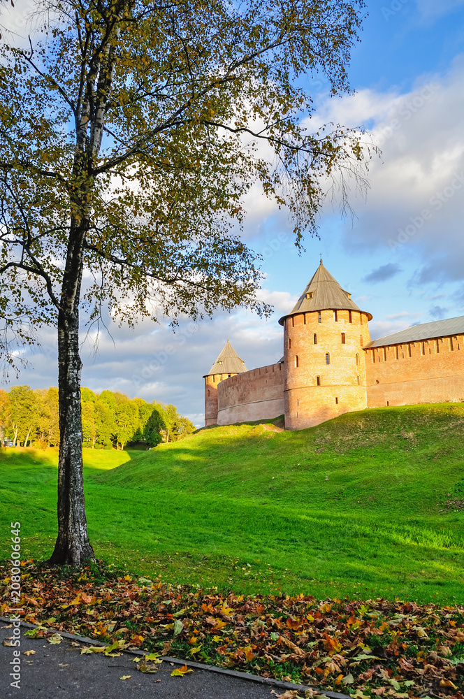 Obraz premium Autumn city landscape - towers and walls of Veliky Novgorod Kremlin on the hill framed by autumn trees under warm sunset light