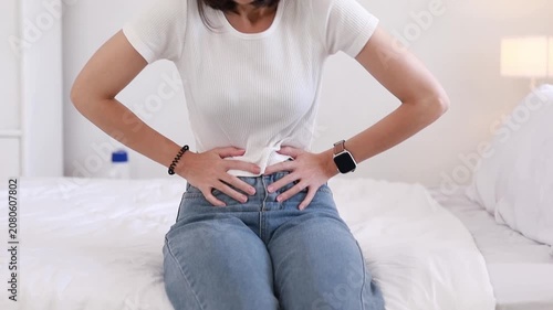 A young woman sat clutching her stomach due to food poisoning, experiencing abdominal pain and intestinal problems such as gastritis or diarrhea while at home.
