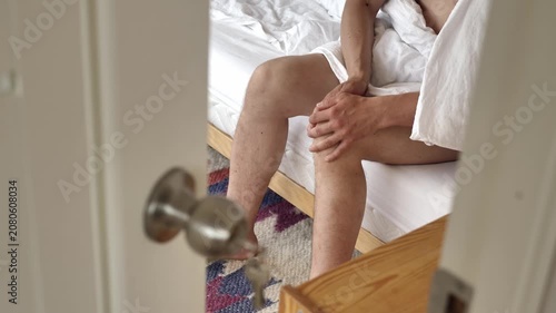 Man holding painful knee while trying to stand up near bed. Medical footage about arthritis, injury and mobility issues