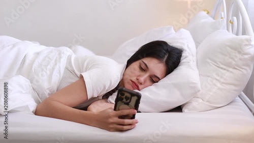 A young woman is using her mobile phone while lying in bed, sending messages and chatting online.