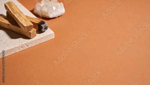 Two palo santo sticks resting on a textured stone slab next to a clear quartz crystal, set against a terracotta background