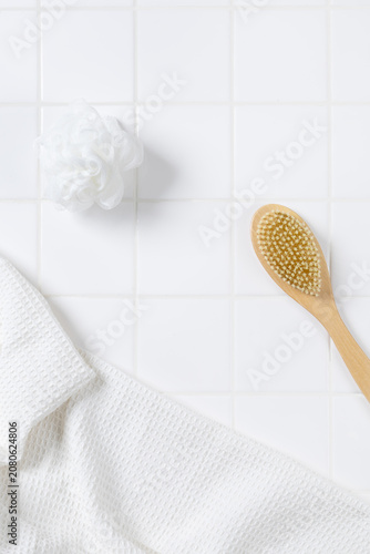 Top view of bathroom product mockup background with copy space. Flat lay of body brush, bath puff, and white towel on square tile wall for cosmetic display.