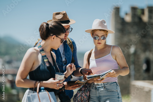 Obraz na plátně Three young tourists consult a map and guidebook while sightseeing at a historic site