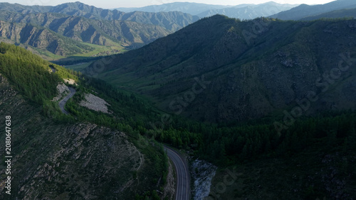 Foto A cinematic drone revealing shot flying over a rocky mountain cleft to uncover a scenic asphalt road and a lush green valley at Chike-Taman Pass in Altai