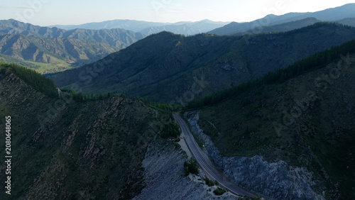 Canvastavla A cinematic drone revealing shot flying over a rocky mountain cleft to uncover a scenic asphalt road and a lush green valley at Chike-Taman Pass in Altai